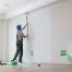 professional painter in a clean room paints interior walls and ceiling white with a long roller brush