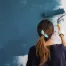 woman using a paint roller to paint blue streaks on home wall