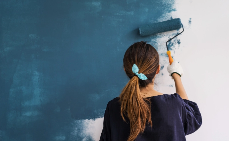 woman using a paint roller to paint blue streaks on home wall